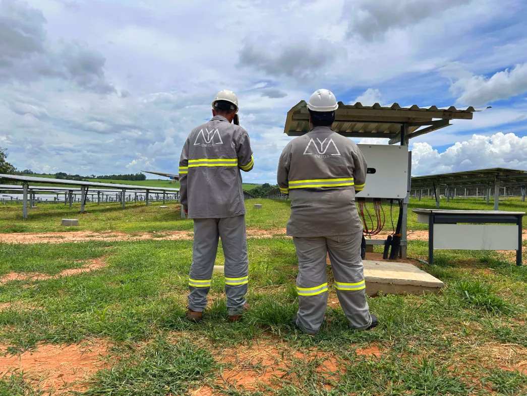 Dois técnicos da AYA Energia em campo, de EPI, ao lado de um inversor